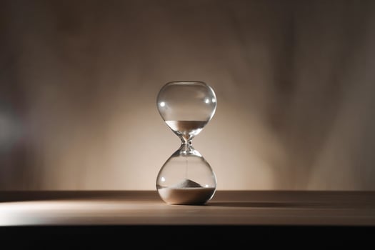 Minimalist Glass time almost over Hourglass on Wooden Surface with Beige Background sidelit low key photo