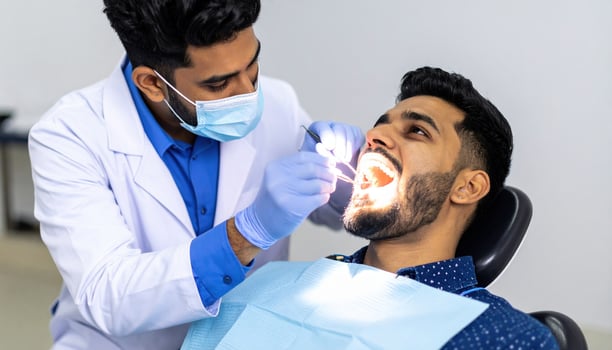 Dentist examines patient teeth dental clinic, using mirror and dental tools to check oral health. patient is sitting dental chair with bib, and dentist is wearing mask and gloves, ensuring hygiene photo
