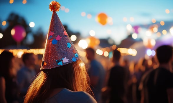 A woman wearing a party hat at an outdoor gathering with a blurred background of lights and people. photo