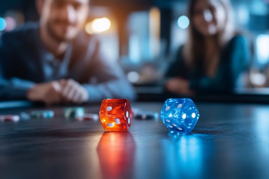 Two dice on a table with a couple in the background, one dice is red and the other is blue. photo