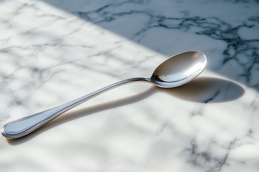 A single, polished silver spoon lays on a white marble surface. The spoon casts a shadow on the surface. photo
