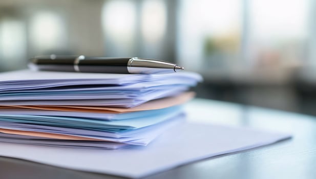 A stack of papers with a pen on top, sitting on a desk photo