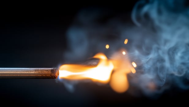 A closeup of a small flame and smoke coming from a metal pipe against a black background. photo