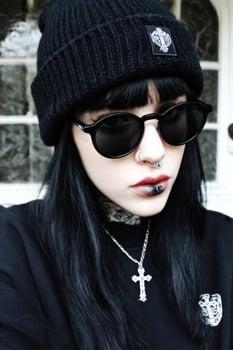 A woman with black hair and piercings wearing a black hat and sunglasses photo