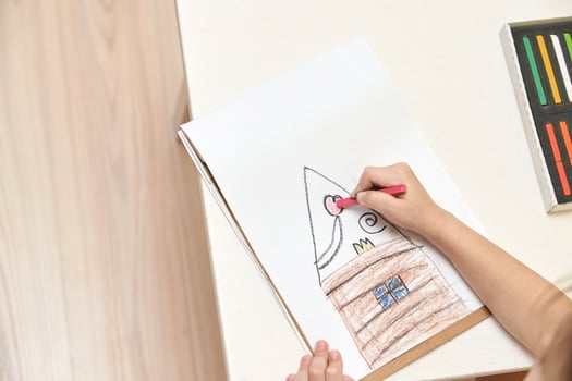Child drawing house with crayons on white paper at home desk. photo
