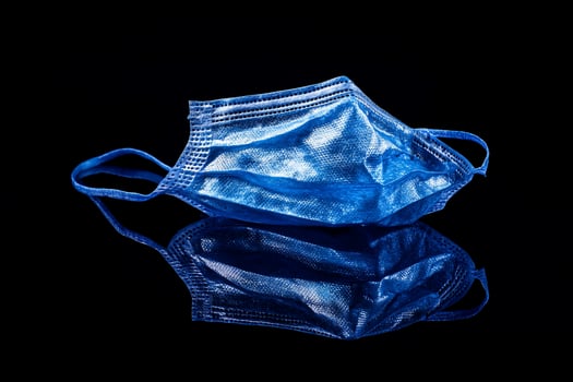 Used blue surgical mask on black reflective surface. photo