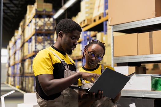African american team preparing merchandise for dispatch in large warehouse, checking inventory on laptop and managing cargo distribution. Sorting packages for logistics infrastructure. photo