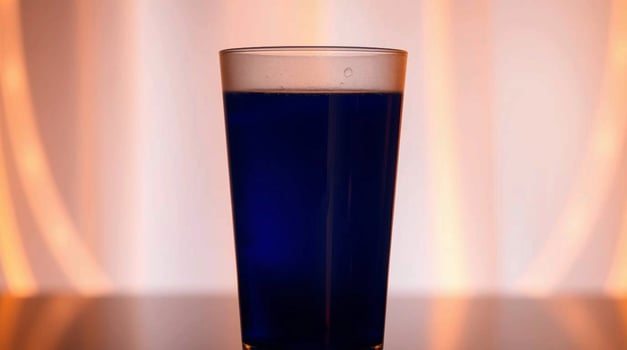 Glass of Deep Blue Liquid Against Warm Background Beverages photo