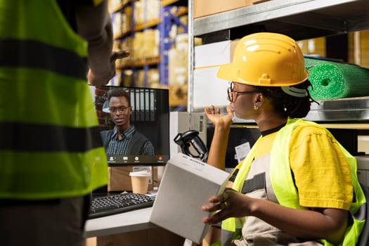 Black female worker chatting with CEO on web online conference, ensuring e-commerce retail activity on computer. Managing order fulfillment with awb tracking info in industrial warehouse. photo