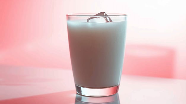 Refreshing Glass of Milk with Ice Cube on Pink Background A Cool Dairy Beverage Image Beverages photo