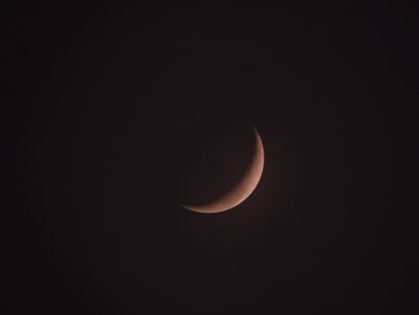 The crescent moon or young moon is pink among the dark sky photo