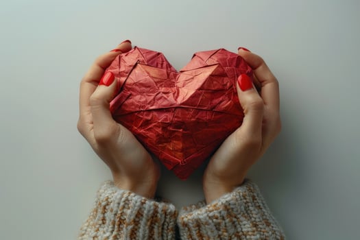 Hands holding red origami heart symbol of love and care affection photo