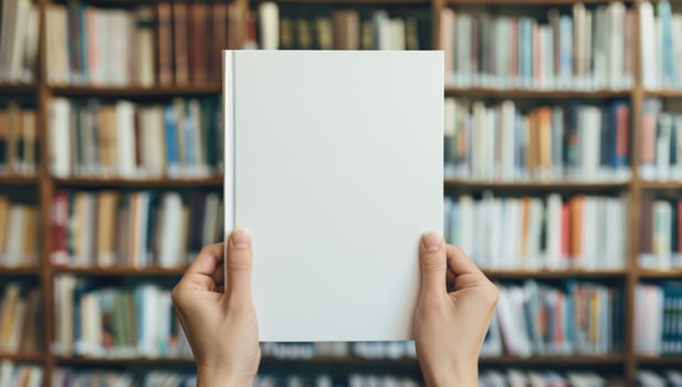 Blank book cover template held in hands for text or graphic overlays with bookshelf background photo