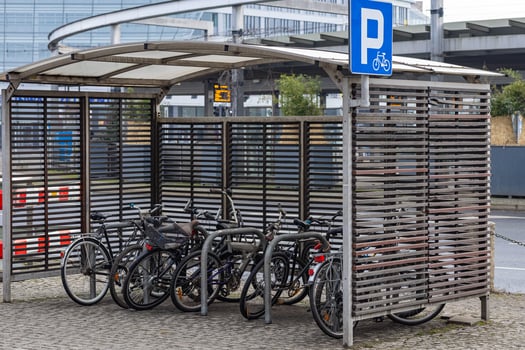 Bicycle parking shelter with multiple bikes locked to metal racks near a modern urban transport hub on a cloudy day. Eco-friendly transport, urban cycling and mobility photo