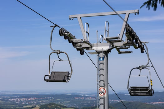 Close-up view of ski lift chair mechanism with cable support tower and pulley system on sunny day. Mountain transport infrastructure, technical engineering and aerial lift operation in summer photo