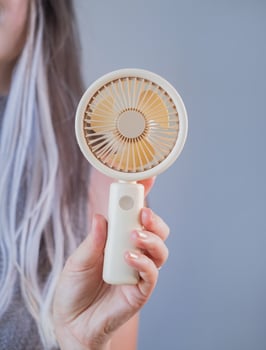 Smiling young woman staying cool with a portable fan while enjoying a warm summer day outdoors. photo