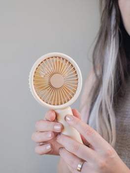Young woman using a compact handheld fan to stay fresh and comfortable outdoors on a hot summer day. photo