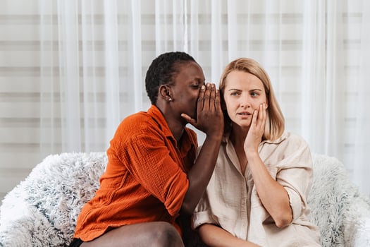 Young woman whispering a secret to her worried friend photo