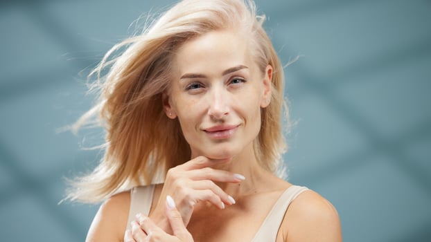 Confident woman with flowing blonde hair gently touching her face, showcasing radiant skin and natural beauty, in a serene spa-like environment, embodying wellness and self-care concepts photo