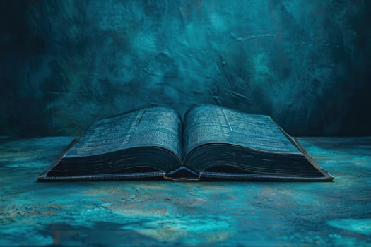 An open antique book on a blue textured surface against a teal blue background. photo