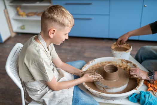 teen boy and instructor shaping clay together at pottery workshop photo