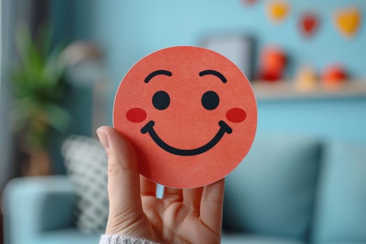 A hand holds up a red smiley face, symbol of happiness. photo