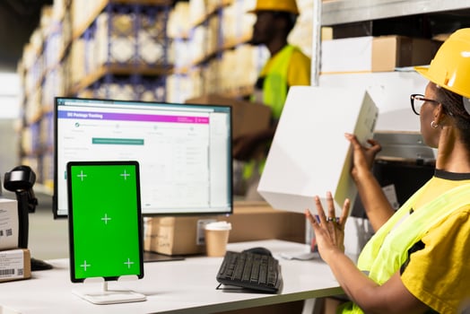 African american staff checking cardboard boxes at desk with chroma key on computer, monitoring parcel status and shipment route via airway bill numbers on pc software. Woman in hi vis vest. photo