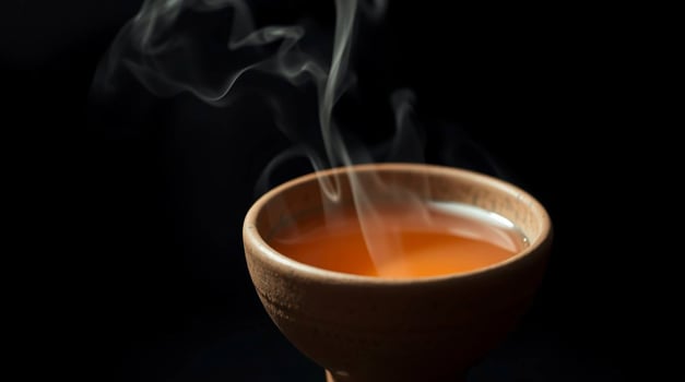 Closeup of a steaming earthenware bowl containing amber liquid against a black background Beverages photo