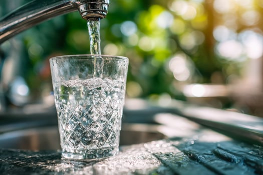 Crystal-clear water filling a textured glass under a flowing tap in natural sunlight photo