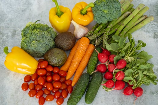 Top view of fresh organic vegetables assortment including broccoli, yellow bell peppers, cherry tomatoes, carrots, cucumbers, radishes, asparagus, garlic and avocados on a light concrete background photo
