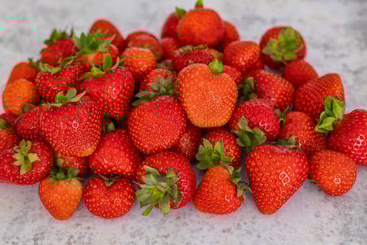 Pile of fresh organic strawberries with vibrant red color and green leaves on a light stone surface, showcasing healthy eating and summer harvest photo
