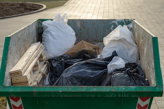 Close-up of green industrial dumpster filled with construction debris, including wooden planks, plastic garbage bags and paper waste, placed outdoors photo