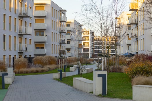 Modern residential apartment complex with green courtyard, paved pathways, landscaped greenery and contemporary architecture illuminated by soft sunlight in an urban setting photo