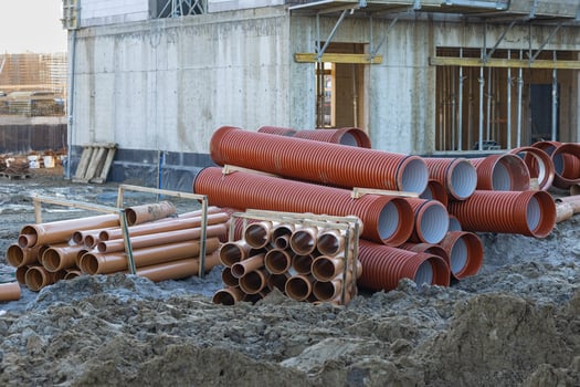 Stacks of construction pipes on a building site with muddy ground and unfinished concrete walls in the background photo