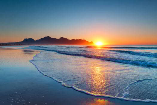 Tranquil sunset over a pristine beach with gentle waves and distant mountains photo