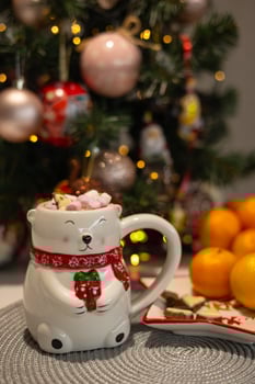 Close-up of a cute polar bear mug set against a decorated Christmas tree with festive ornaments. Concept of cozy winter holidays, warm drinks, and festive home atmosphere. photo