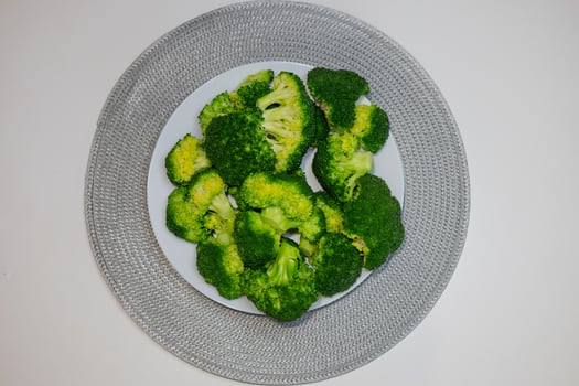 Top view of fresh green broccoli florets served on a white plate with a decorative silver placemat. Concept of healthy eating, plant-based diet, and organic food preparation photo