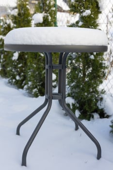 Snow-covered outdoor round table in a garden on a cold winter day. Concept of winter season, outdoor furniture, and snowy weather in the backyard photo