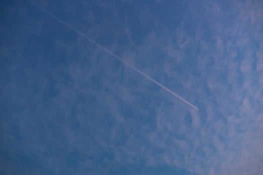Airplane flying across the sky leaving a long vapor trail against a soft blue and pink cloud backdrop during evening. Concept of travel, aviation, and peaceful sky scenery photo