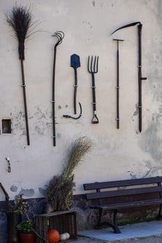 Old wooden and metal farming tools hanging on a rustic wall next to a bench on a sunny day. Concept of vintage agricultural equipment, traditional tools, and rural life photo