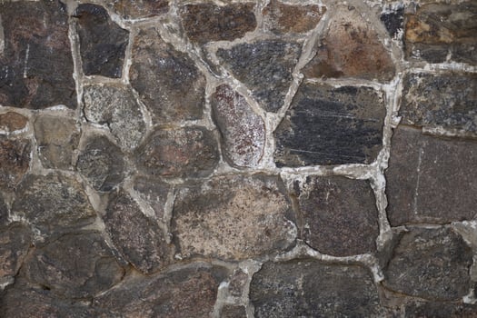 Close-up of a natural stone wall with textured surface on a sunny day. Concept of architecture, construction materials, and rustic outdoor backgrounds photo