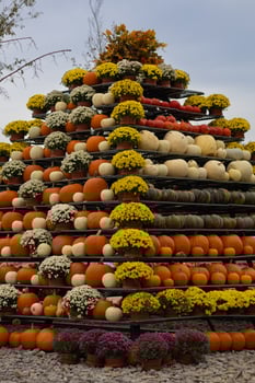 Pyramid-shaped display of pumpkins and colorful flowers arranged in pots for an autumn harvest festival on a cloudy day. Seasonal decoration, fall harvest and festive outdoor events photo