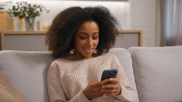 Happy carefree cheerful gadget addict African American girl female woman using mobile phone media smartphone chatting browsing scrolling gadget enjoying cyberspace application shopping online at home photo