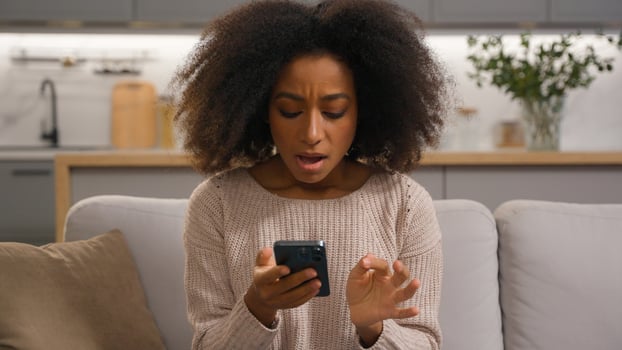 Sad shocked upset frustrated African American woman reading bad news lost failure with mobile phone female at home living room disappointed girl reject notification scam smartphone problem error app photo