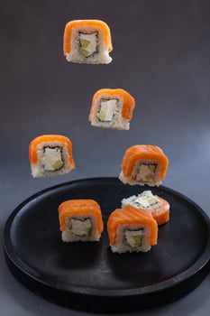 Floating salmon sushi roll with cream cheese and avocado in mid-air over dark plate. Japanese cuisine, creative food presentation, and culinary artistry in motion photo