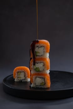 Stack of sushi rolls drizzled with soy sauce on a black plate in a minimalist setting. Concept of Japanese cuisine, fresh ingredients, and food presentation photo