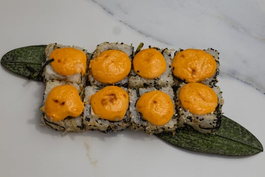 Spicy sushi rolls with creamy topping served on a green leaf and white plate under natural light. Asian cuisine, seafood delicacies and artistic food presentation photo