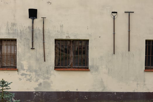 Old tools hanging on a weathered building wall with barred windows. Concept of rural lifestyle, gardening equipment, and vintage architecture in an outdoor setting photo