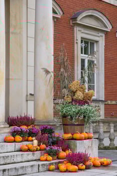 Autumn porch decoration with vibrant pumpkins, colorful flowers, and dry grass in wooden barrel on stone steps building. Concept of seasonal outdoor decor, fall harvest and festive autumn atmosphere photo