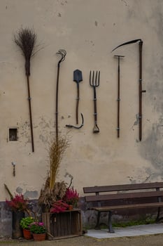 Vintage farming tools hanging on rustic wall with potted plants and a bench. Concept of traditional agriculture, rural lifestyle and old-fashioned craftsmanship photo